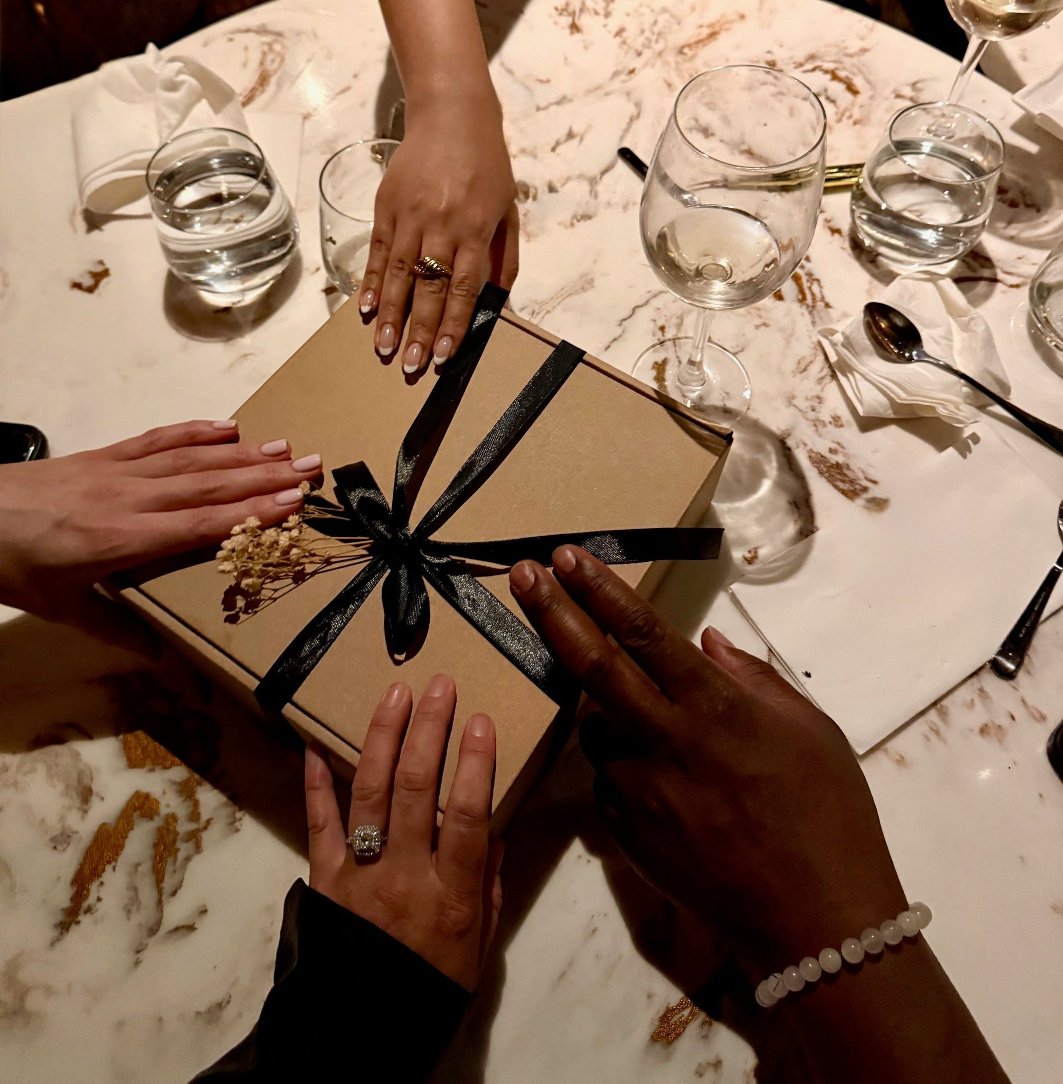 Four people holding a gift box with a black ribbon on a marble table.