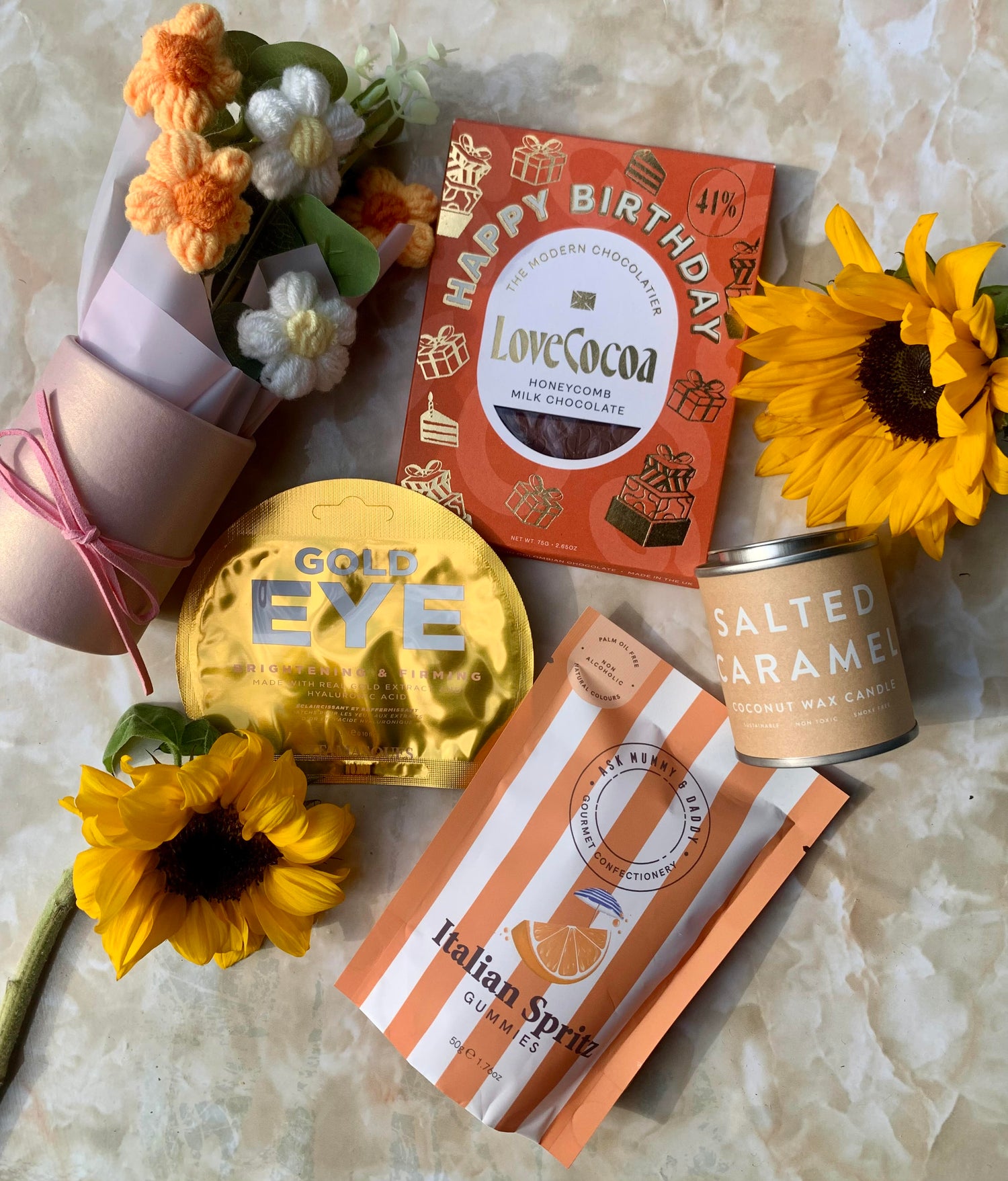 birthday box, happy birthday chocolate, salted caramel candle, gold eye gel mask, italian spritz alcohol free gummies and orange and white crotchet flower bouquet