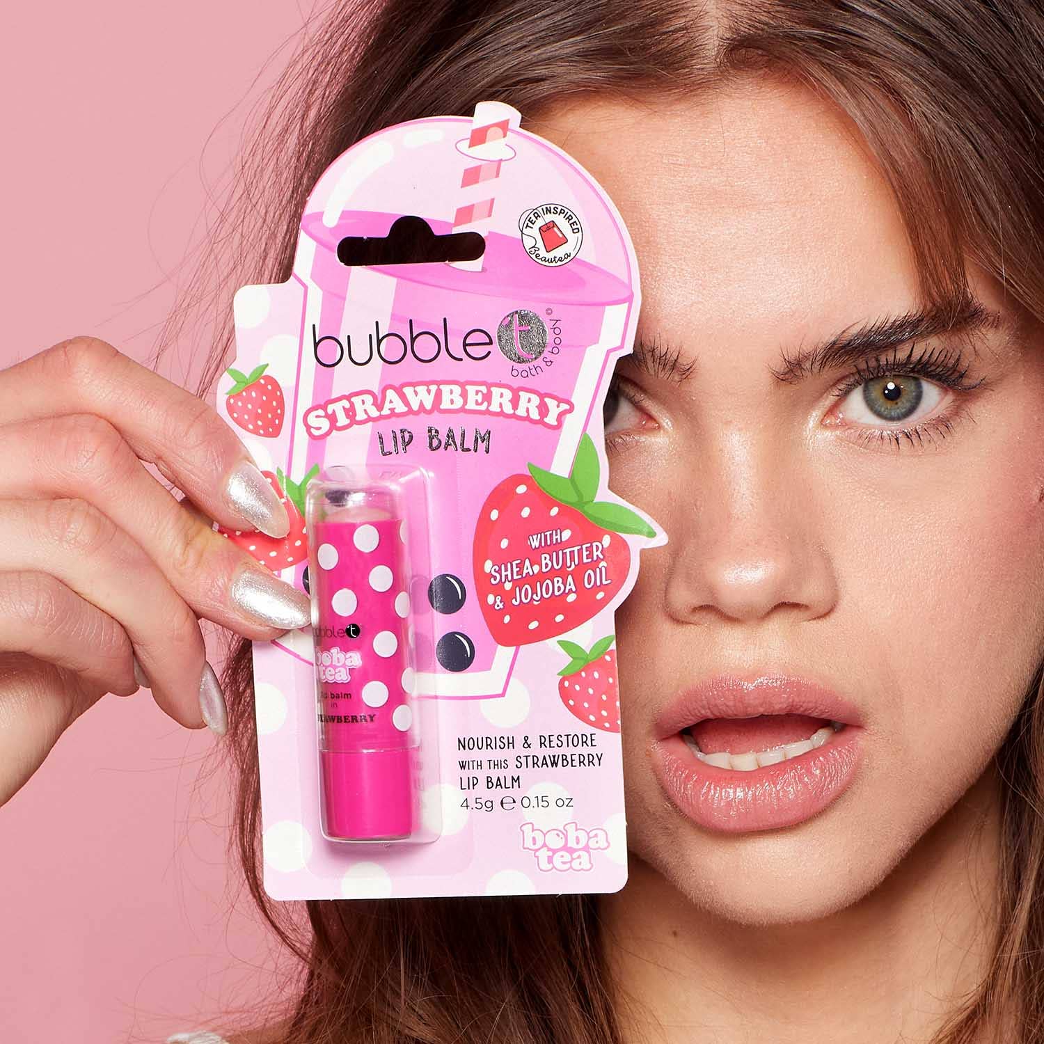 Person holding a pink strawberry lip balm with packaging against a pink background