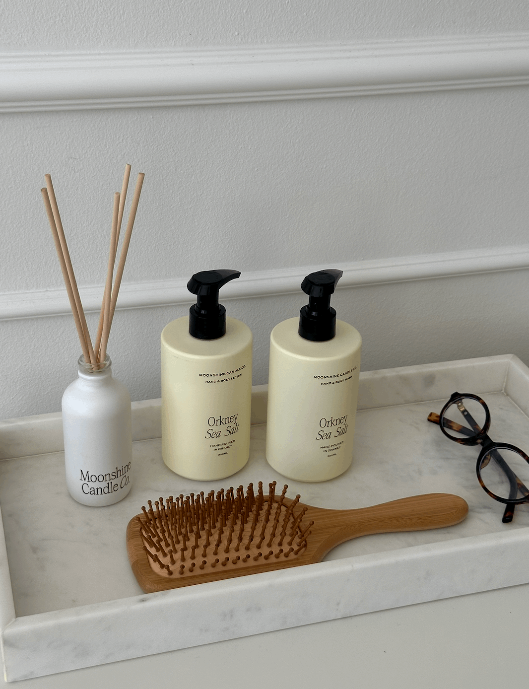 Two bottles of 'Orchid Sea Salt' shampoo and conditioner, a wooden hairbrush, and a small bottle labeled 'Moonlight Candle Co.'