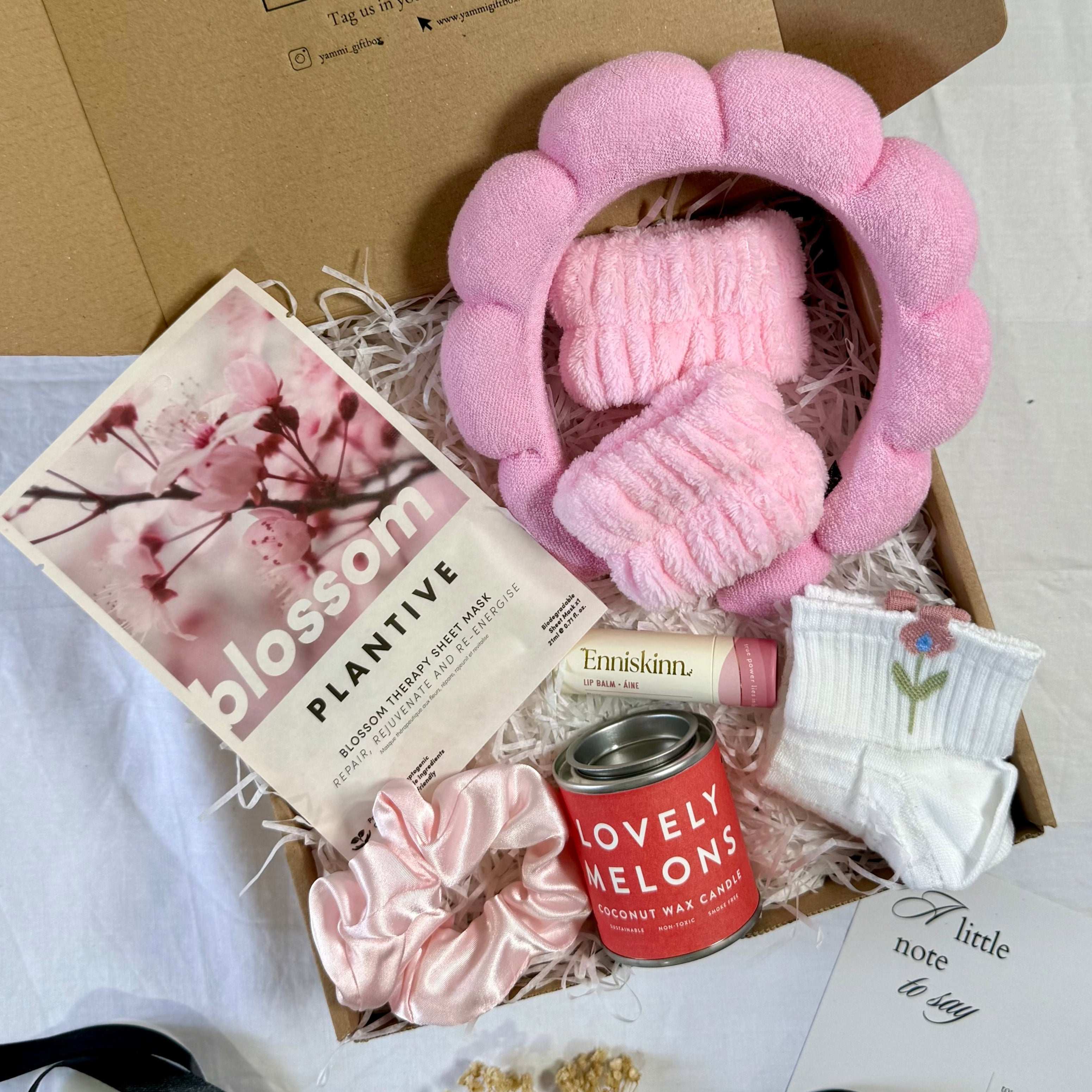 Yumm Gift Box with pink plush head band,  skincare product, and other items on a white surface.