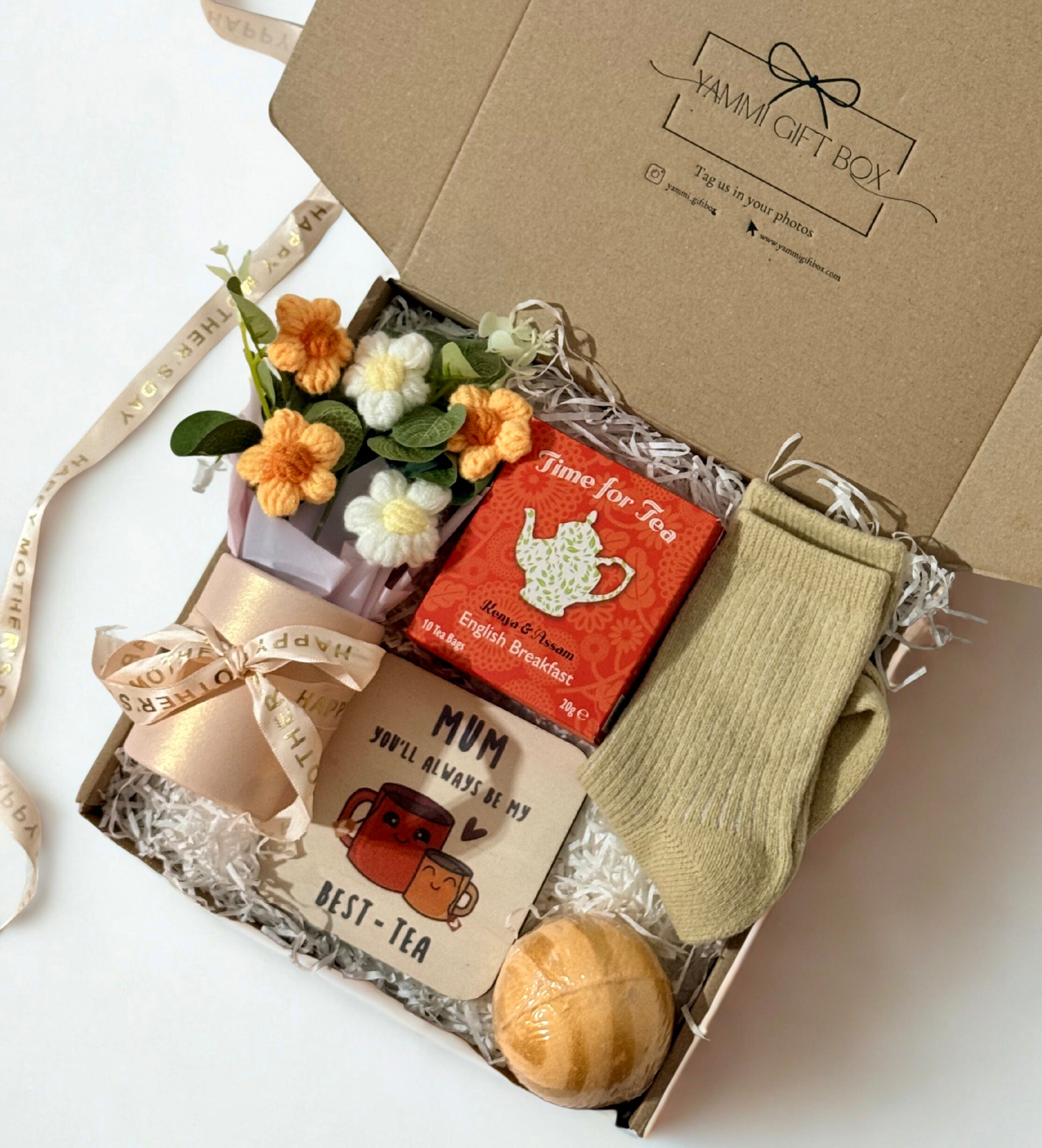 Gift box with tea-themed items including a tea bag, socks, and a small crotchet flower.