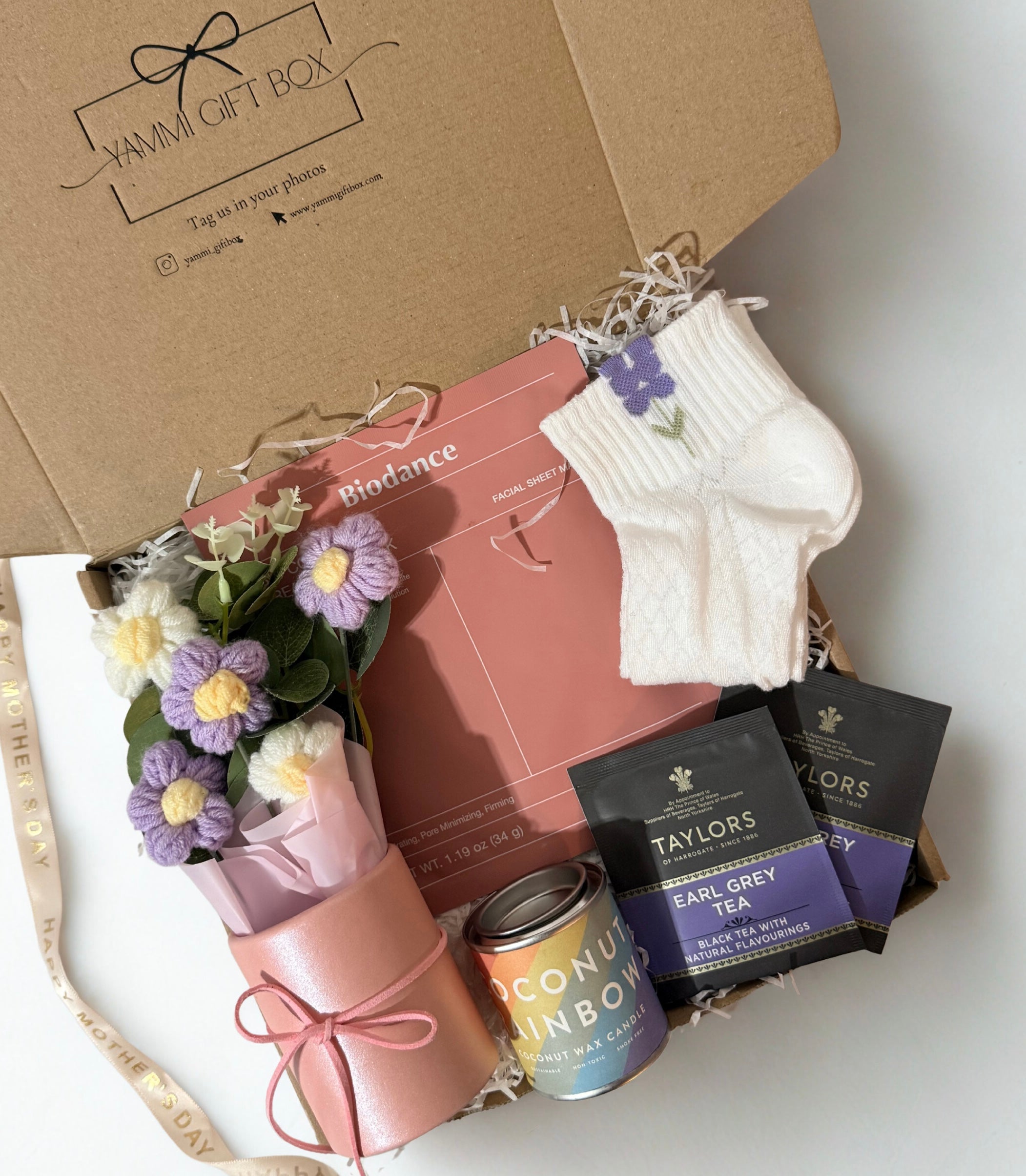 Gift box with flowers, tea, and socks on a white surface