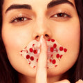 Close-up of a woman's face with a decorative paper over her mouth featuring red cherries.