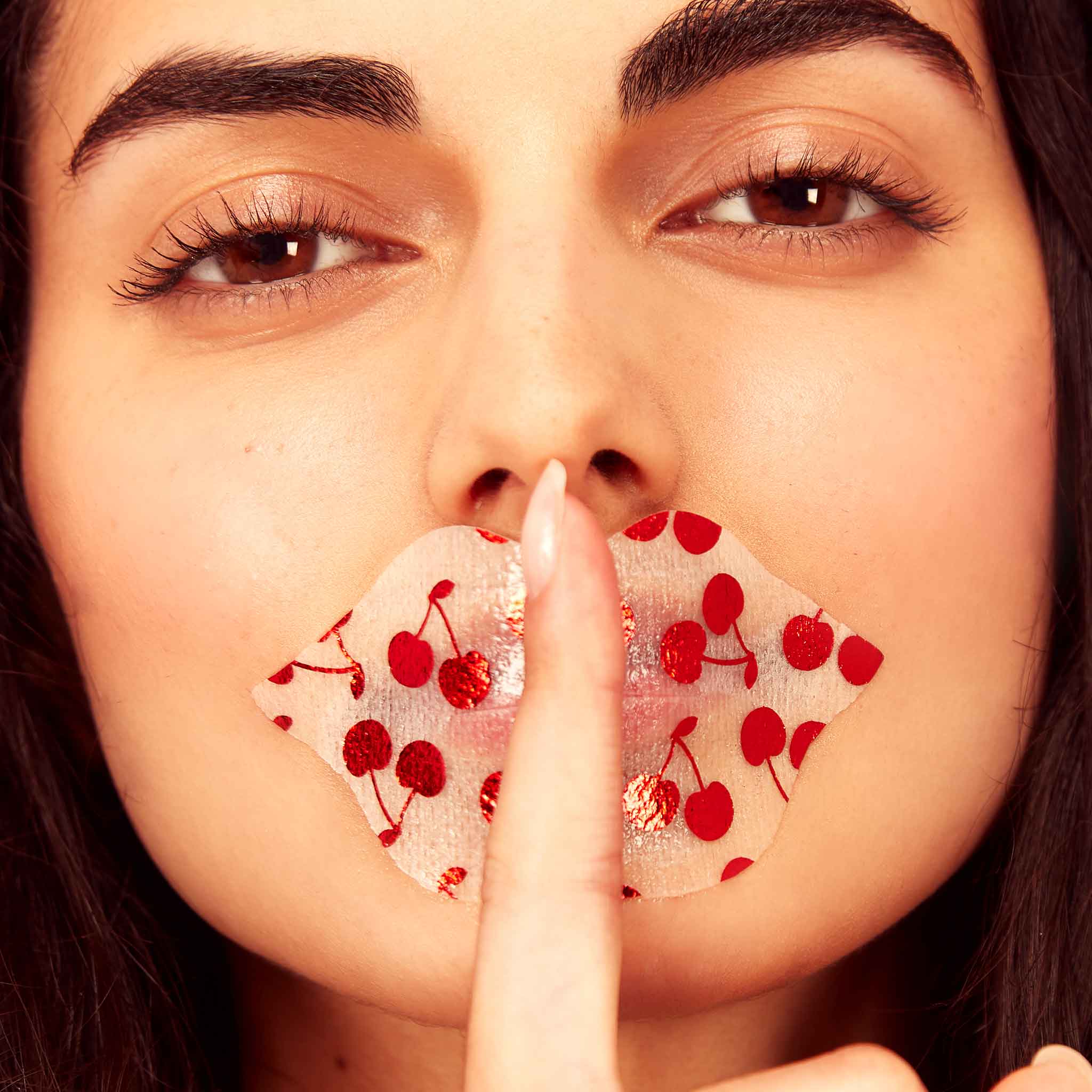 Close-up of a woman's face with a decorative paper over her mouth featuring red cherries.