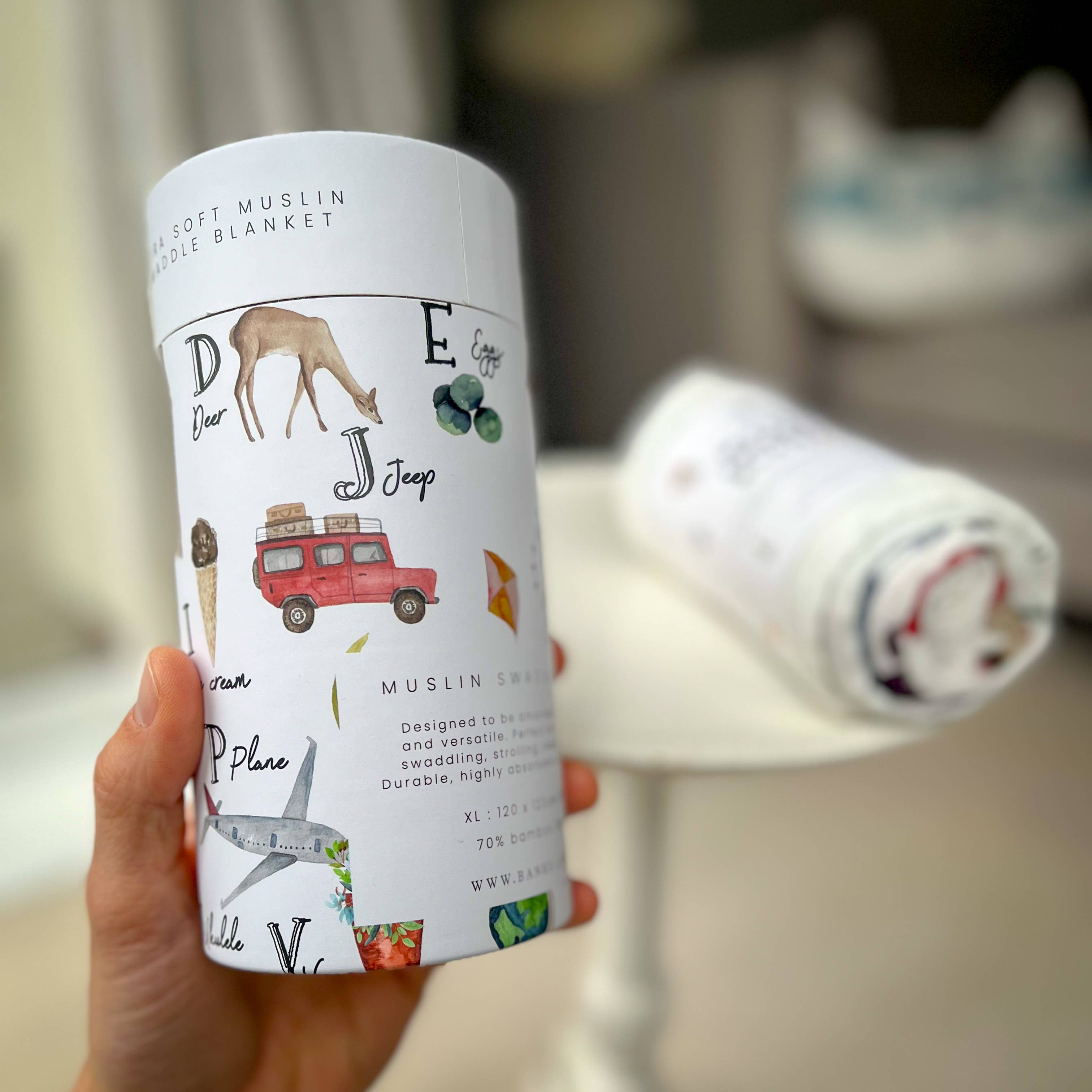 Person holding a muslin blanket packaging with travel-themed illustrations.