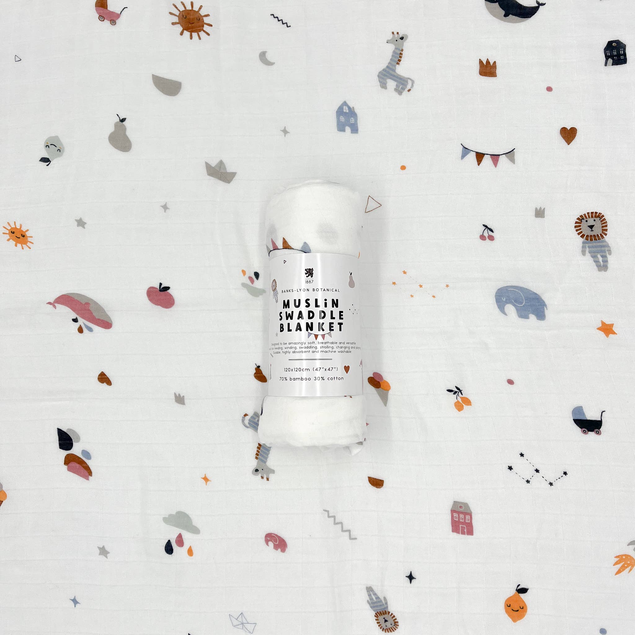 White muslin swaddle blanket with colourful whimsical illustrations including elephants, apples, rain clouds, suns, houses, lions, bunting, and stars — wrapped roll in centre labeled "Muslin Swaddle Blanket" by Banks Lyon Botanical.