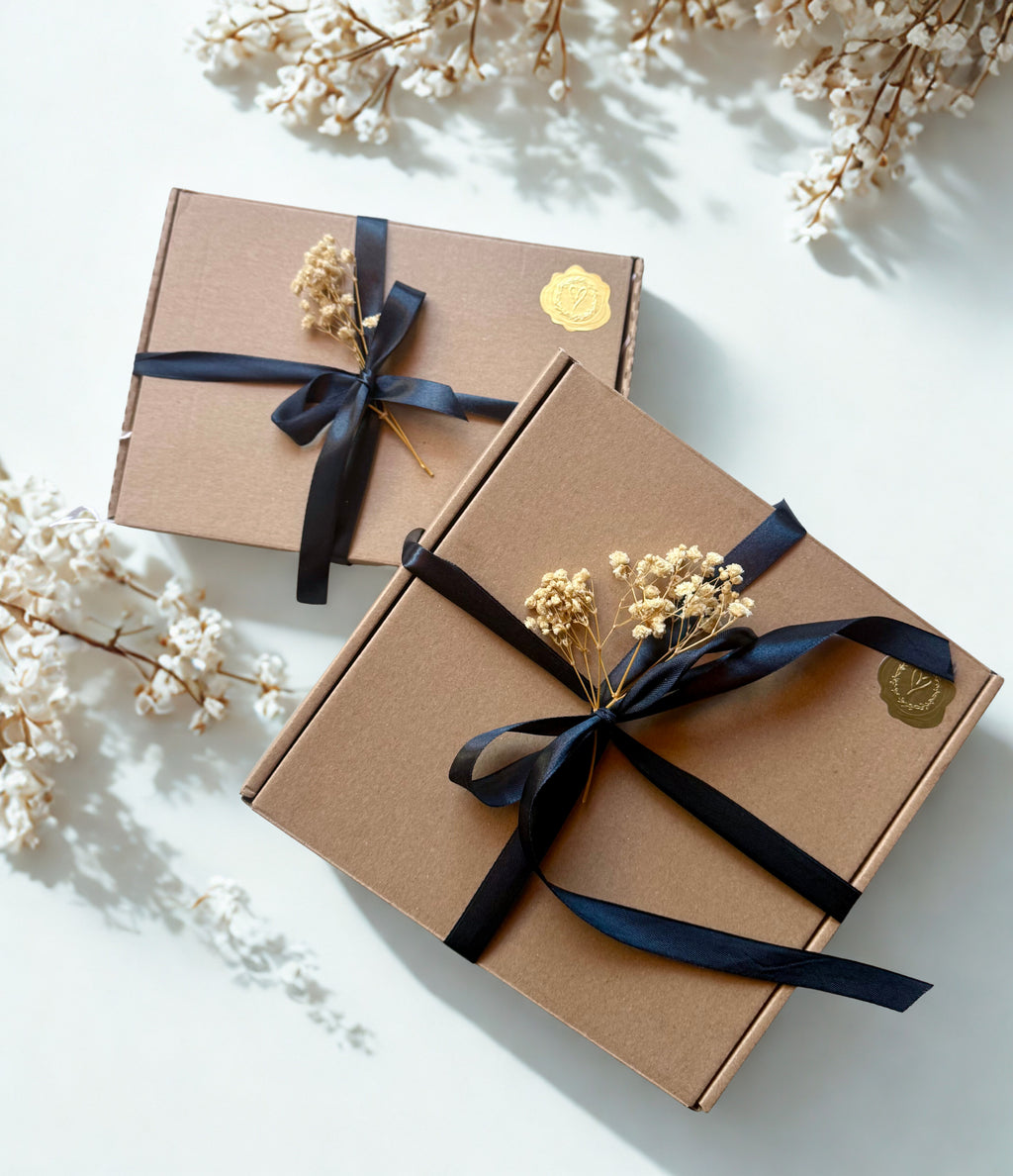 Two brown gift boxes with black satin ribbons and dried flowers on a light background
