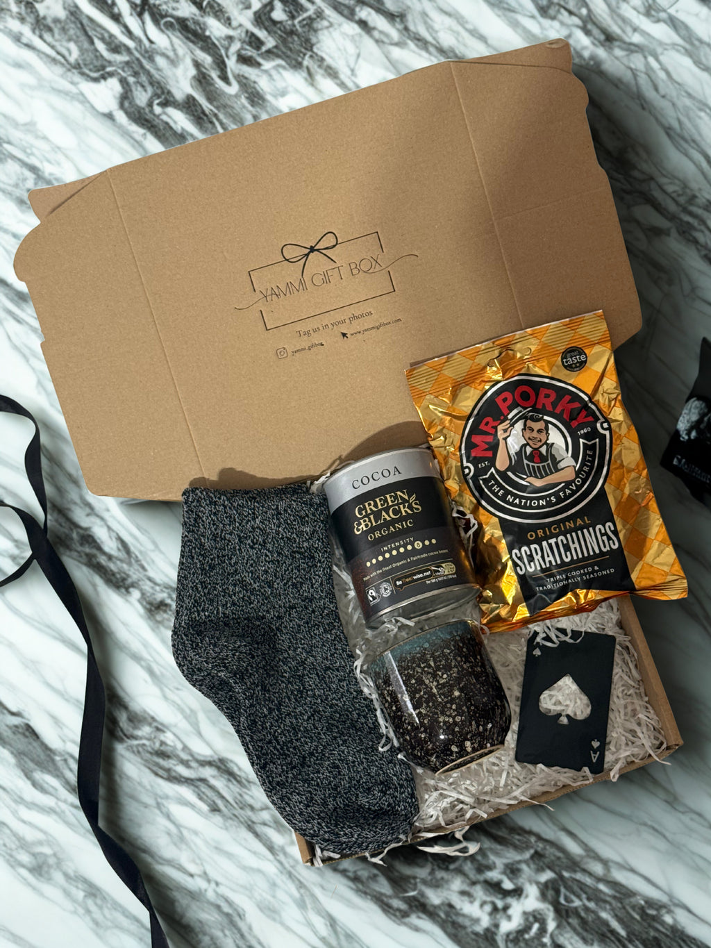 Men's gift box with socks, hot chocolate, and snack and cup on a marble surface