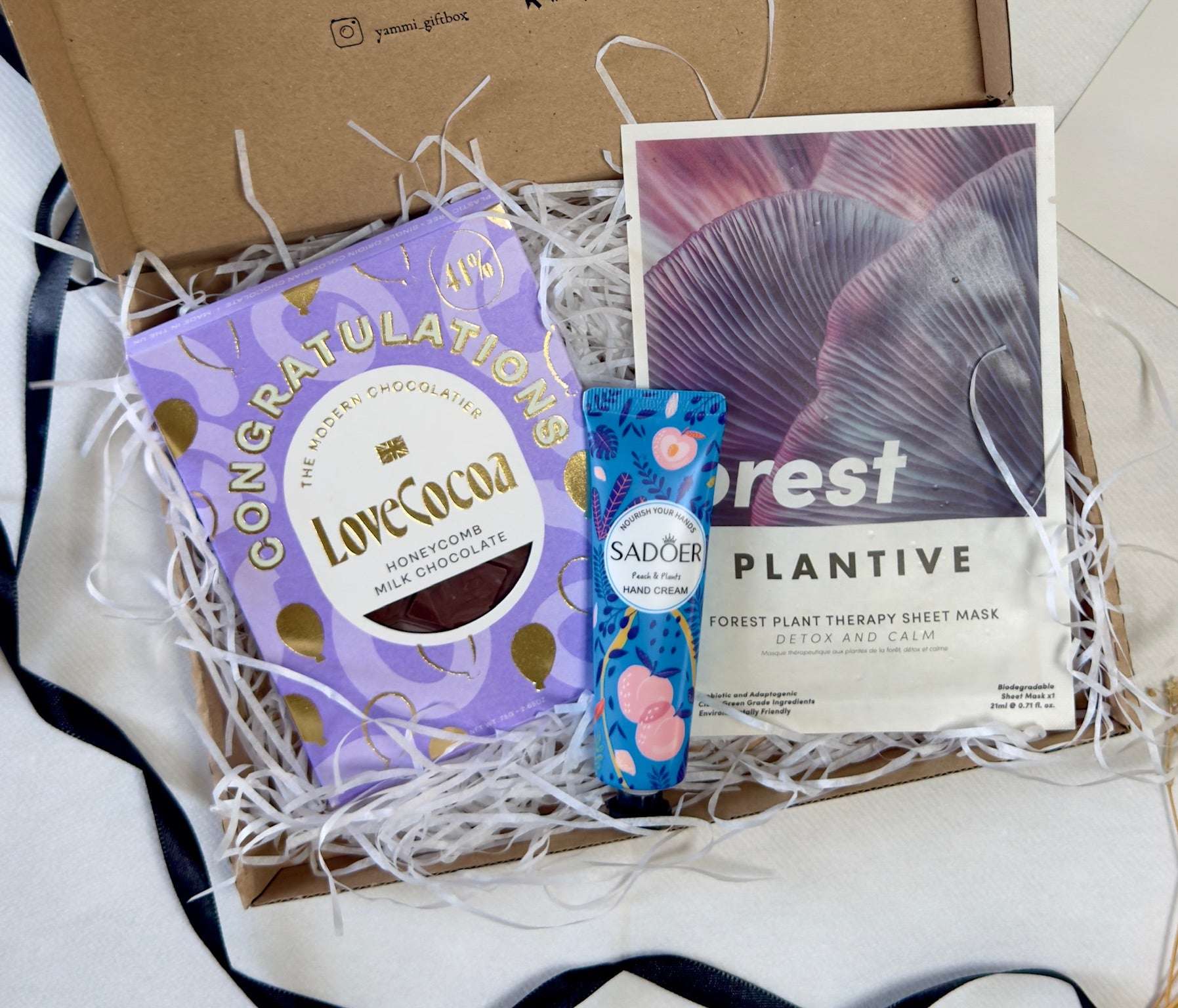 Box with chocolate bar, skincare product, and plant-based sheet mask.