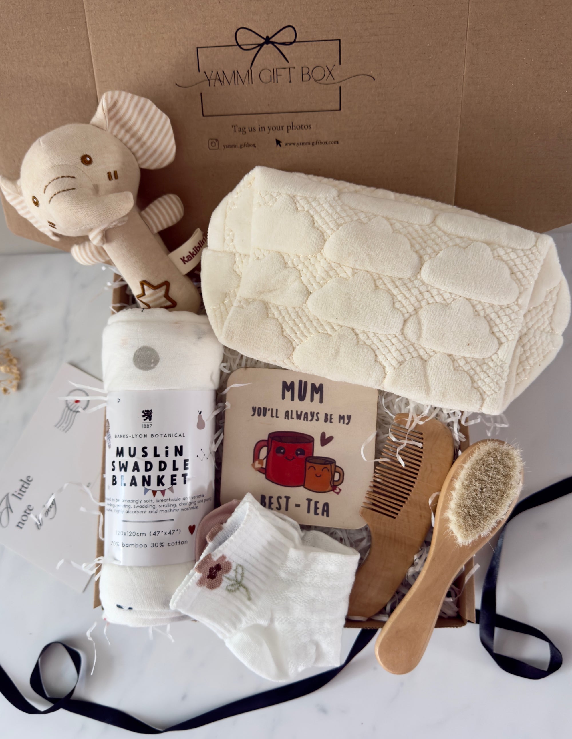 New Mum and Baby gift box including a soft muslin swaddle blanket, plush elephant toy, cream cloud-patterned knitted blanket, ‘Mum you’ll always be my best-tea’ keepsake card, baby hairbrush, wooden comb, and baby socks with floral embroidery – neatly presented in a Yammi Gift Box.