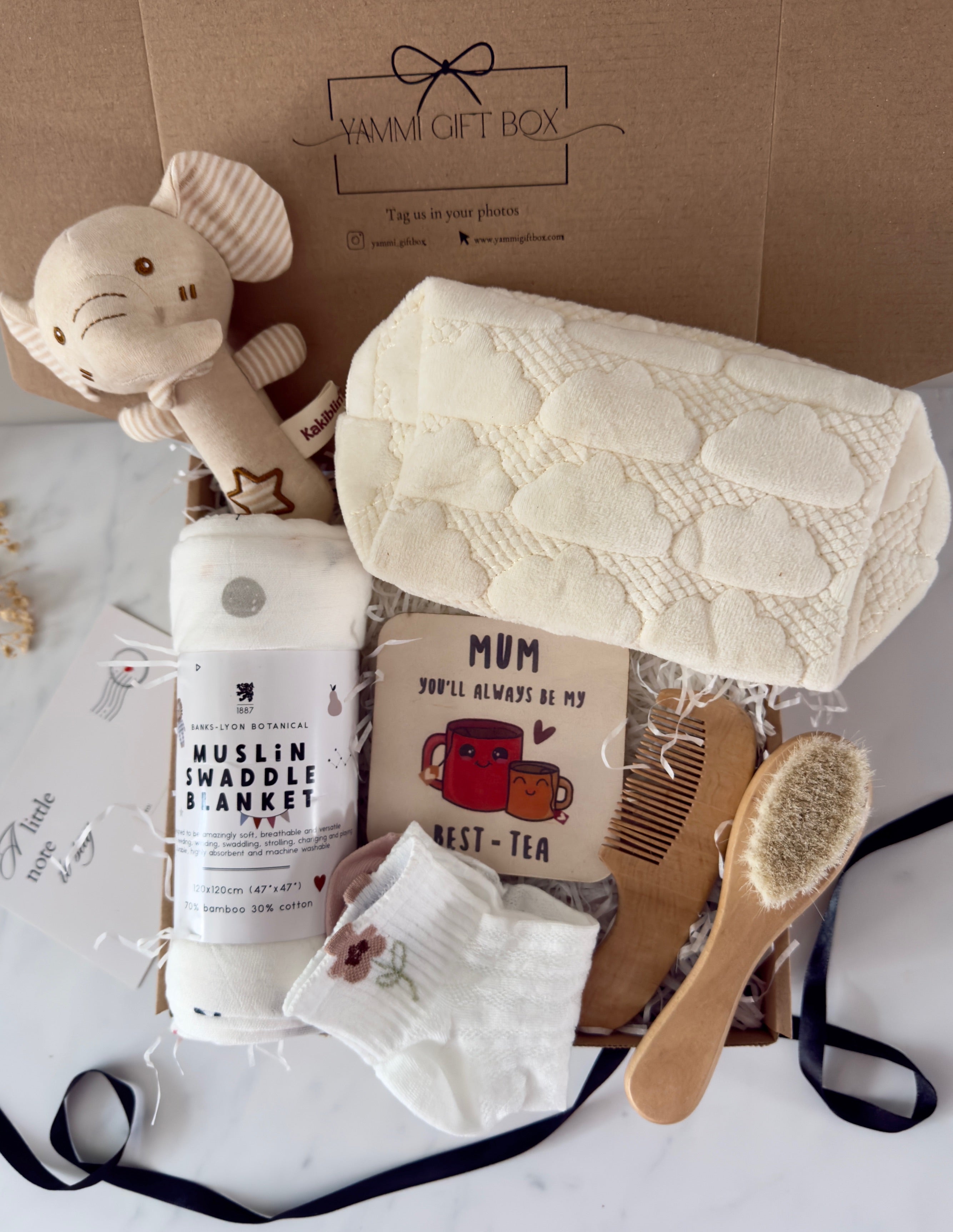 New Mum and Baby gift box including a soft muslin swaddle blanket, plush elephant toy, cream cloud-patterned knitted blanket, ‘Mum you’ll always be my best-tea’ keepsake card, baby hairbrush, wooden comb, and baby socks with floral embroidery – neatly presented in a Yammi Gift Box.