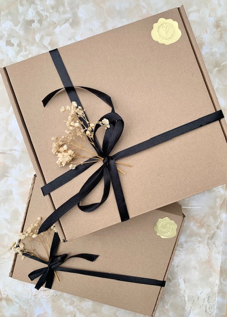 Two brown gift boxes with black ribbons and small flowers on a light background