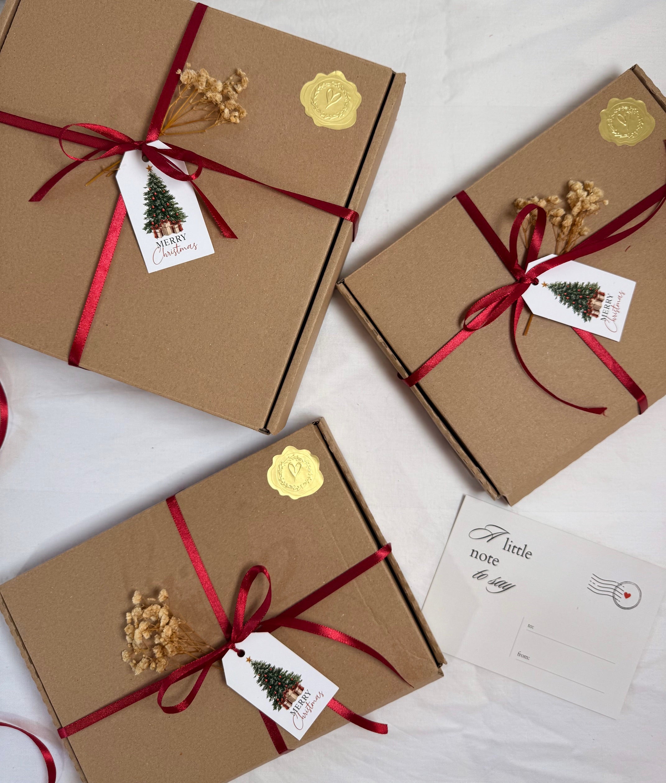 Three brown gift boxes with red ribbons and Christmas-themed tags on a light background.