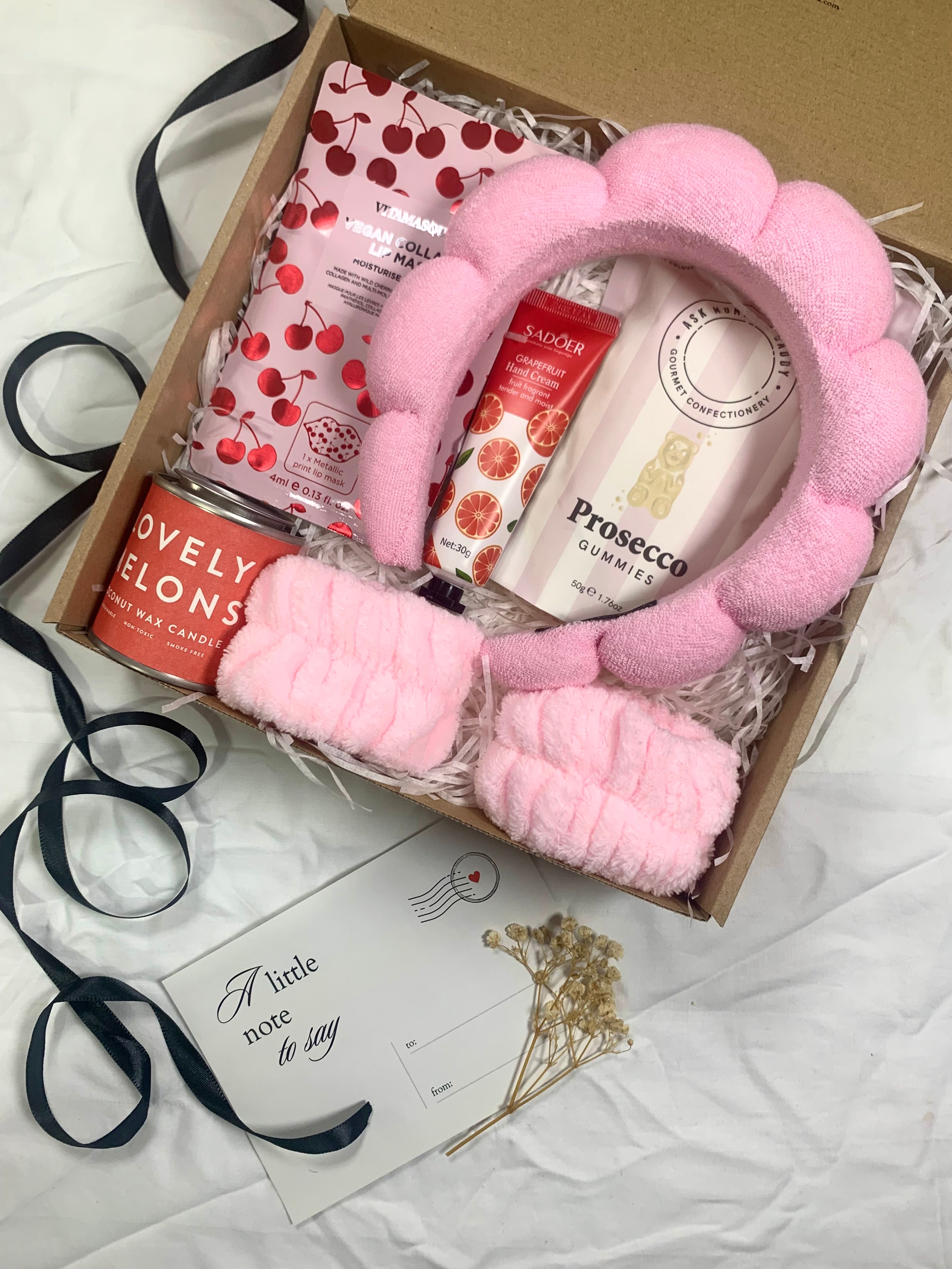 Pamper gift box for her with pink fluffy flower headband, cherry face mask, hand cream, Prosecco gummies, and Lovely Melons tin candle.