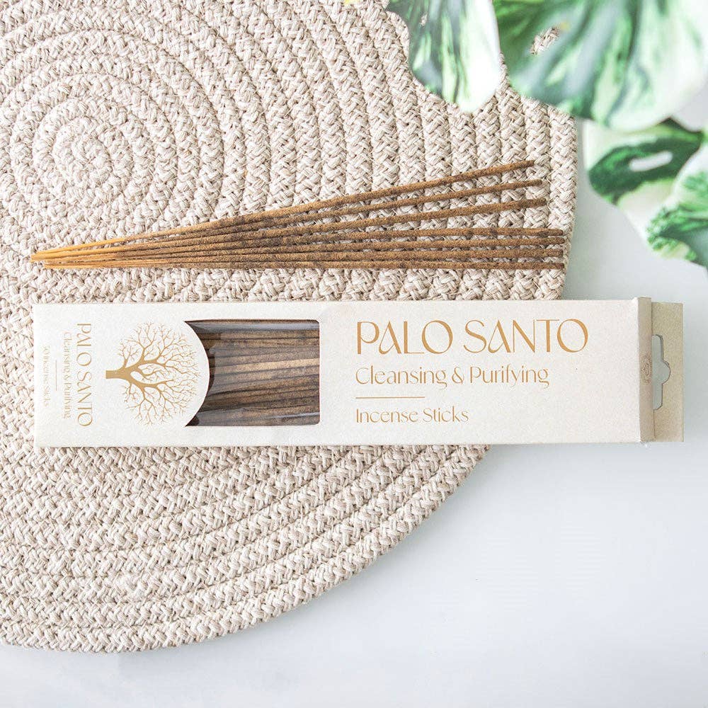 Elegant cream-colored rectangular packaging for Palo Santo incense sticks, featuring a gold tree emblem on the left and bold gold lettering on the right that reads “PALO SANTO – Cleansing & Purifying – Incense Sticks.” A transparent window reveals the wooden sticks inside, and the overall design conveys a clean, natural, and spiritual aesthetic.