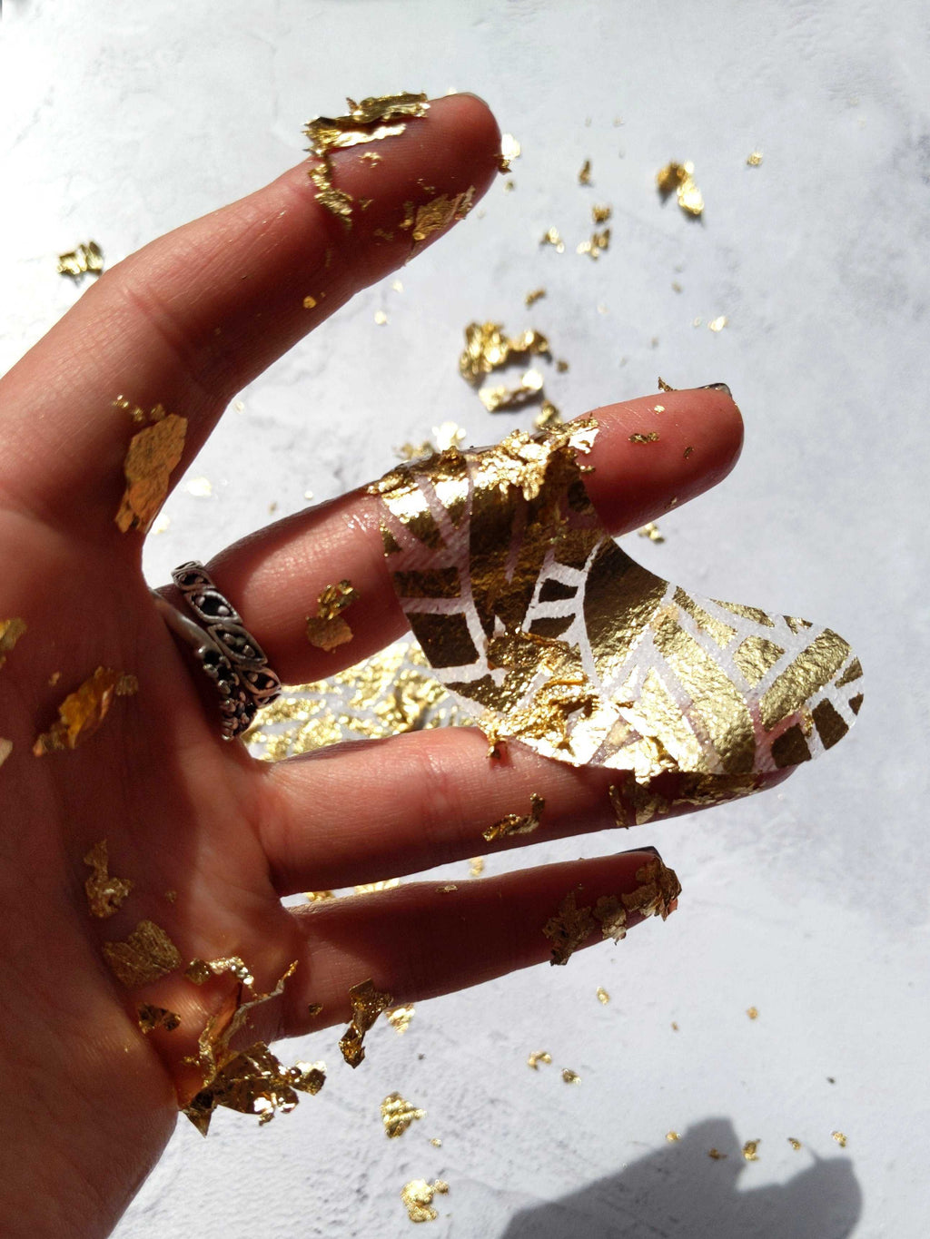 Hand with gold leaf on nails and fingers against a light background